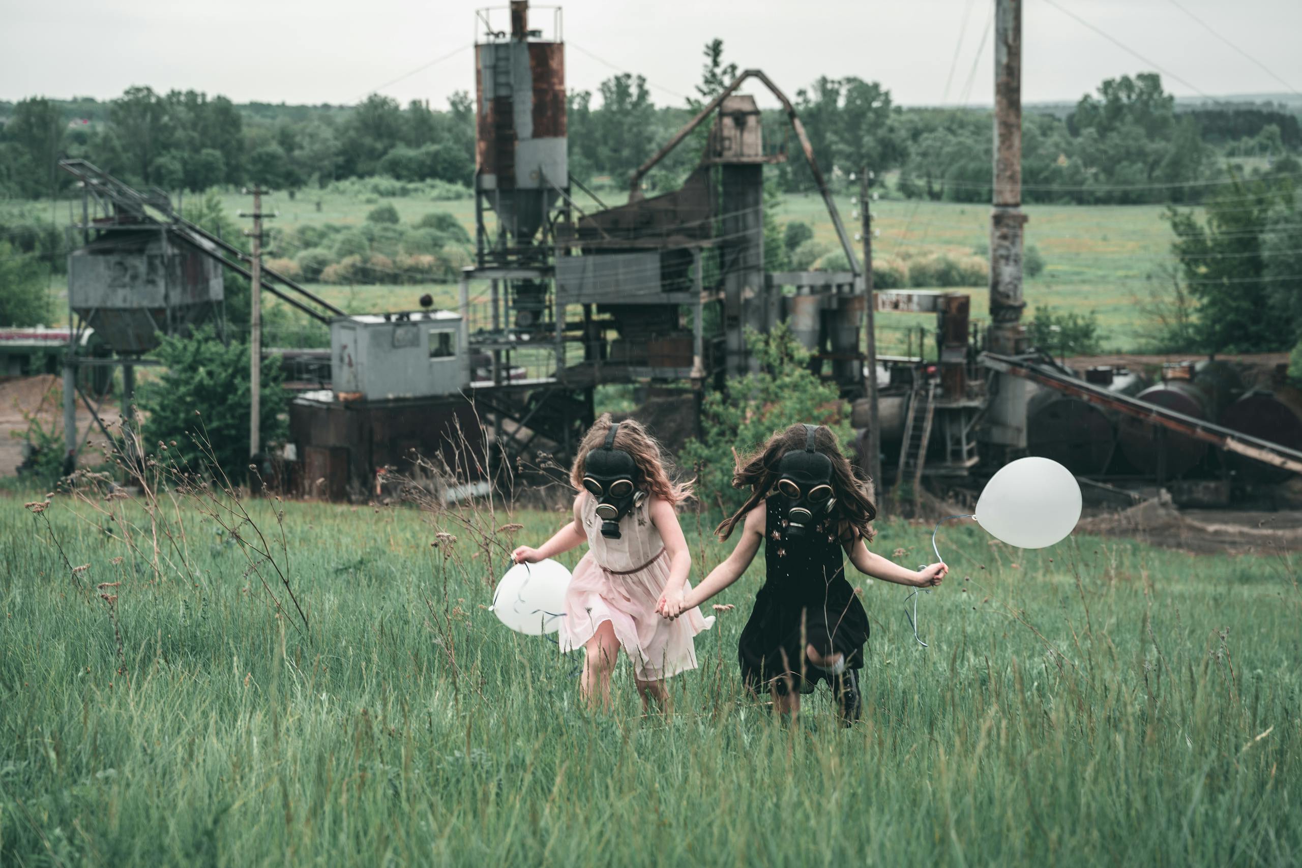 Two children wearing gas masks run with balloons near an industrial site.