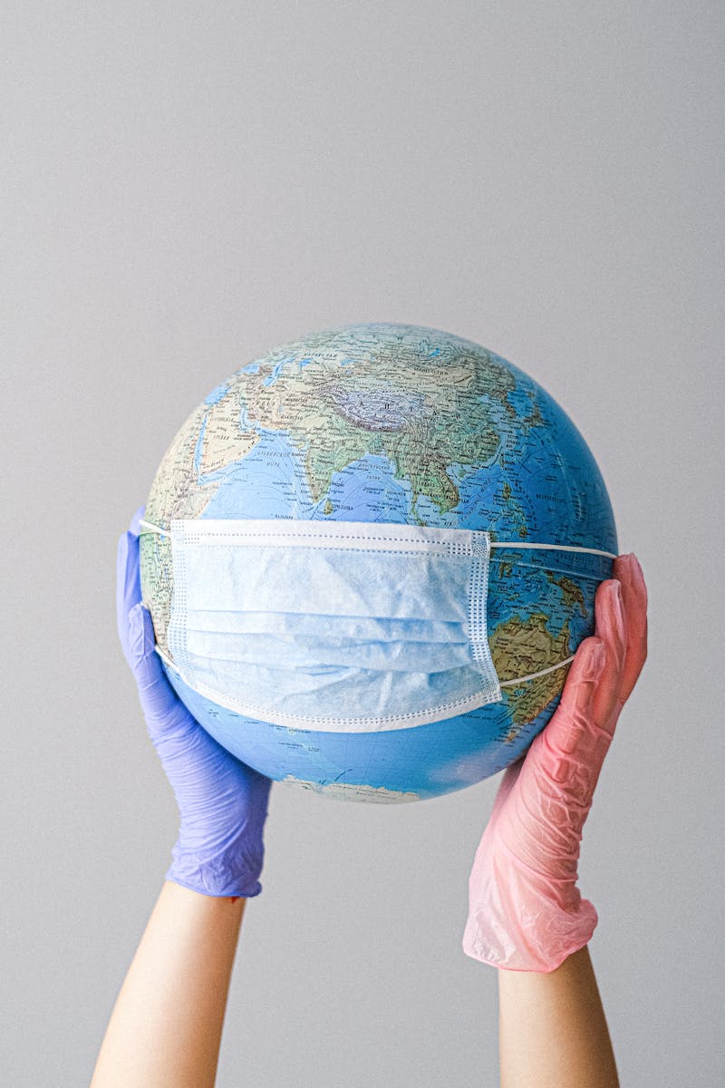 Hands in gloves holding a globe with a mask, symbolizing global health and pandemic protection.